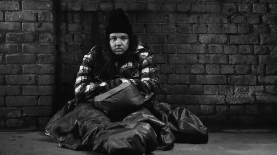 A black and white photo of Mia, sitting huddled in a sleeping bag in a dark street