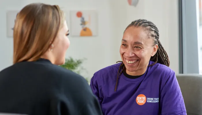 A person wearing a Centrepoint t-shirt smiles during a positive conversation with a young homeless person