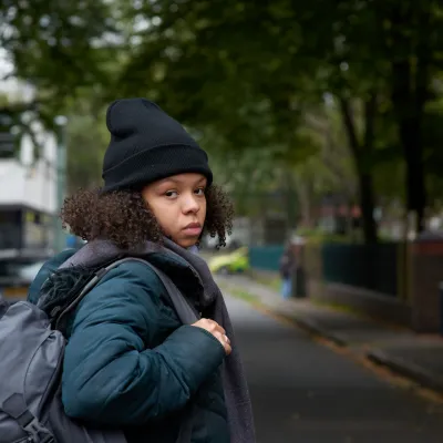 A young homeless person carries a backpack outside on a chilly day